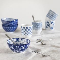 several blue and white bowls with spoons on a table cloth next to utensils