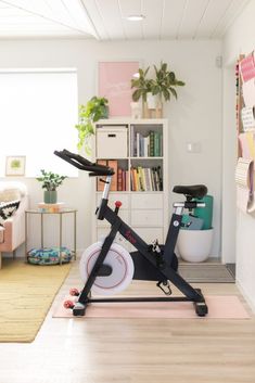 an indoor exercise bike in the corner of a room with bookshelves and plants