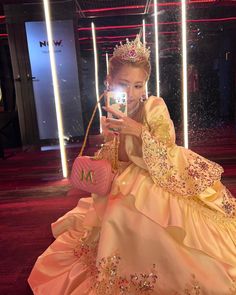 a woman in a princess dress taking a selfie with her cell phone while wearing a tiara