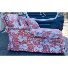 a red and white chair sitting on top of a sidewalk next to a blue car