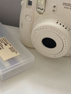 a white polaroid camera sitting on top of a table next to a plastic container