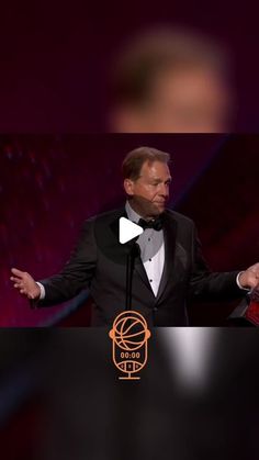 a man in a tuxedo standing at a podium with his hands out to someone