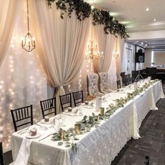 a long table is set up with white linens and greenery for an elegant wedding reception