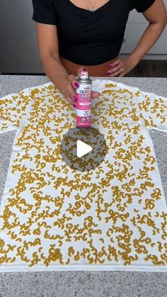 a woman is holding a spray bottle over a t - shirt that has yellow and white flowers on it