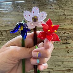 a hand holding three glass flowers on top of a wooden table