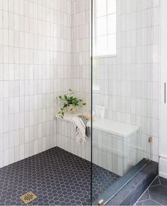 a white tiled bathroom with black and white flooring, glass shower door and window