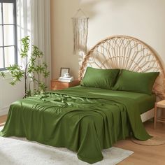 a bed with green sheets and pillows in a room next to a plant on the floor