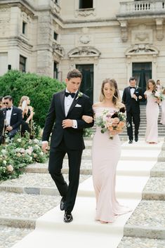 the bride and groom are walking down the stairs at their wedding ceremony in front of an elegant building