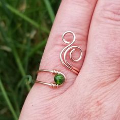 a person's hand holding a ring with a green stone on it and two wire wrapped around the ring