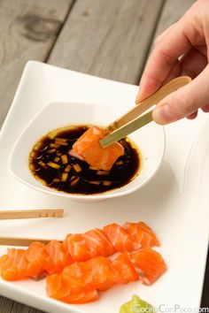 someone is cutting up some sushi on a white plate with chopsticks and sauce