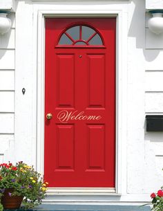 a red front door with welcome written on it and potted flowers in the foreground