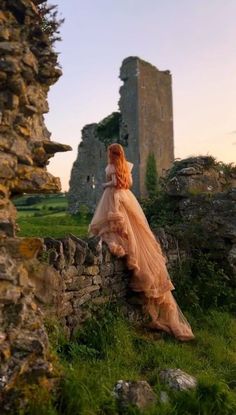 a woman in an orange dress leaning against a stone wall and looking into the distance