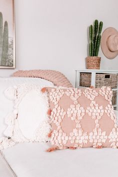 a white bed topped with pillows next to a green plant and potted cacti