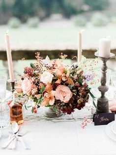 a centerpiece with flowers and candles is displayed on a table in front of an outdoor setting