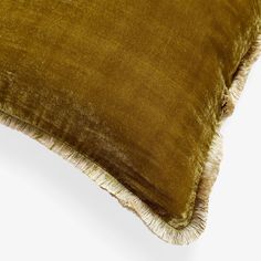 a brown velvet pillow with fringes on the bottom and sides, sitting on a white surface