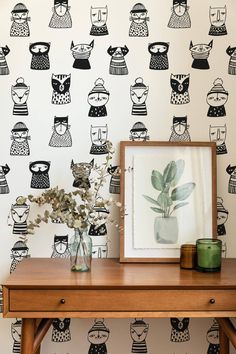 a wooden table topped with a vase filled with flowers next to a wall covered in black and white cats