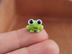 a tiny green frog with big eyes sitting on someone's finger