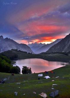 the sun is setting over a mountain lake with mountains in the background and tents set up on the grass