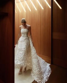 a woman in a white wedding dress standing by a wooden wall with lights on it