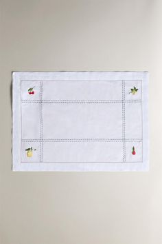 an embroidered placemat with apples and cherries on white linen, hanging from a wall