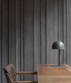 a wooden table with a lamp on top of it next to a chair in front of a wall