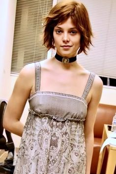 a woman wearing a dress and choker standing next to a chair in an office