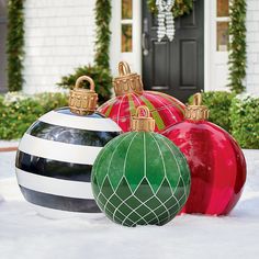 three christmas ornaments sitting in the snow near a house with wreaths and garland on it