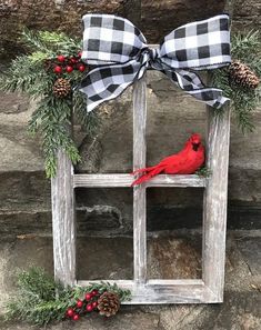 a red bird sitting on top of a wooden window frame with pine cones and berries