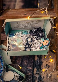 an open box with various items in it sitting on a wooden table next to string lights