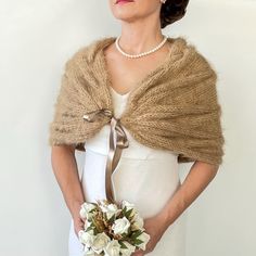 a woman in a white dress holding a bridal bouquet and wearing a shawl