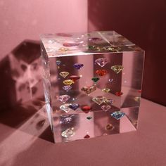 a clear cube with many different colored diamonds on it's sides, sitting in front of a pink wall