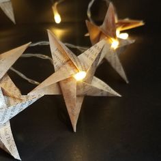 two paper stars with lights on them sitting next to each other in front of a black background