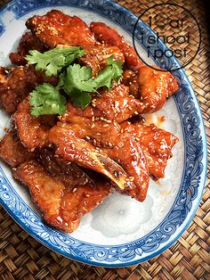 a blue and white plate topped with chicken wings covered in teriyaki sauce, garnished with cilantro