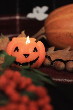 a pumpkin shaped candle sitting on top of a table next to leaves and acorns