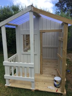 a small wooden shed with the door open and paint bucket on the ground next to it