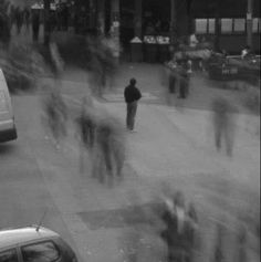 black and white photograph of people walking down the street in front of buildings with cars