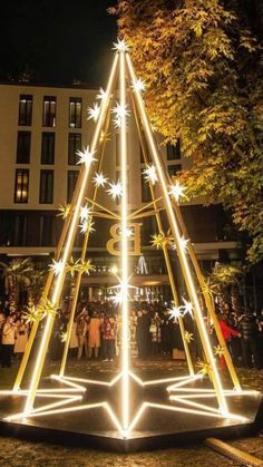 a lighted christmas tree in the middle of a park at night with people standing around it