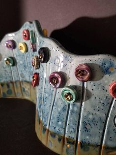 two ceramic sculptures with colorful buttons on them sitting side by side in front of a wall