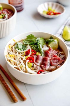 a white bowl filled with meat and veggies next to chopsticks on a table