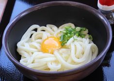 a bowl with noodles, an egg and scallions in it on a table