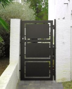 an open black gate in front of a white wall and palm tree on the other side