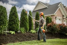 a man using a hedge trimmer in front of a house on a cloudy day