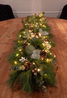 a long table with pine cones and greenery on it, lit up by christmas lights