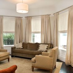 a living room filled with furniture and windows covered in beige drapes, along with two couches