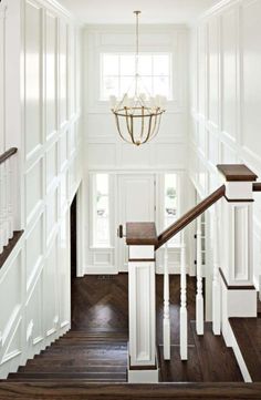 the stairs in this house are white and have wood treading on each side, with a chandelier hanging from the ceiling