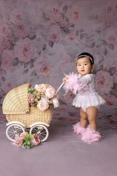 a baby girl in a white dress is pushing a stroller with flowers on it