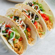 three tacos with shredded chicken, black beans, lettuce and tomatoes on them