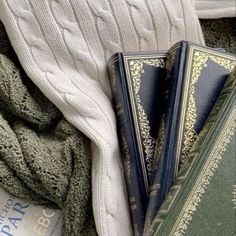 three books sitting on top of a blanket next to a pile of sweaters and blankets