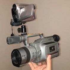 a person holding a camera in front of a video camera on a tripod with two microphones attached to it