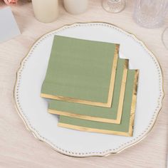 four green napkins on a white plate with gold trim around the edges, sitting on a wooden table